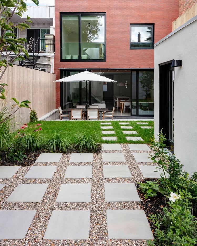 Diseño de patio trasero urbano con adoquines Techo-Bloc Industria 600 en un diseño de cuadrícula limpia con juntas de grava decorativas, muebles de patio modernos y una fachada de ladrillo rojo.