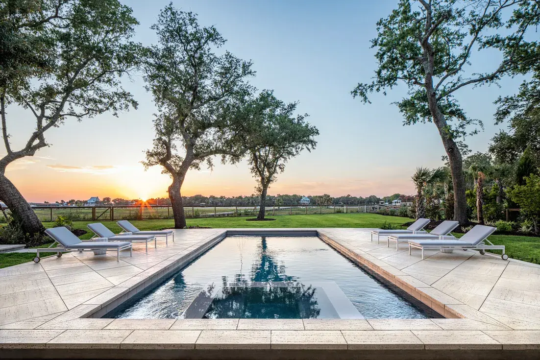 Losa Travertina Marfil de Techo-Bloc con acabado cepillado, creando un patio moderno y elegante junto a la piscina con un paisaje rural escénico.